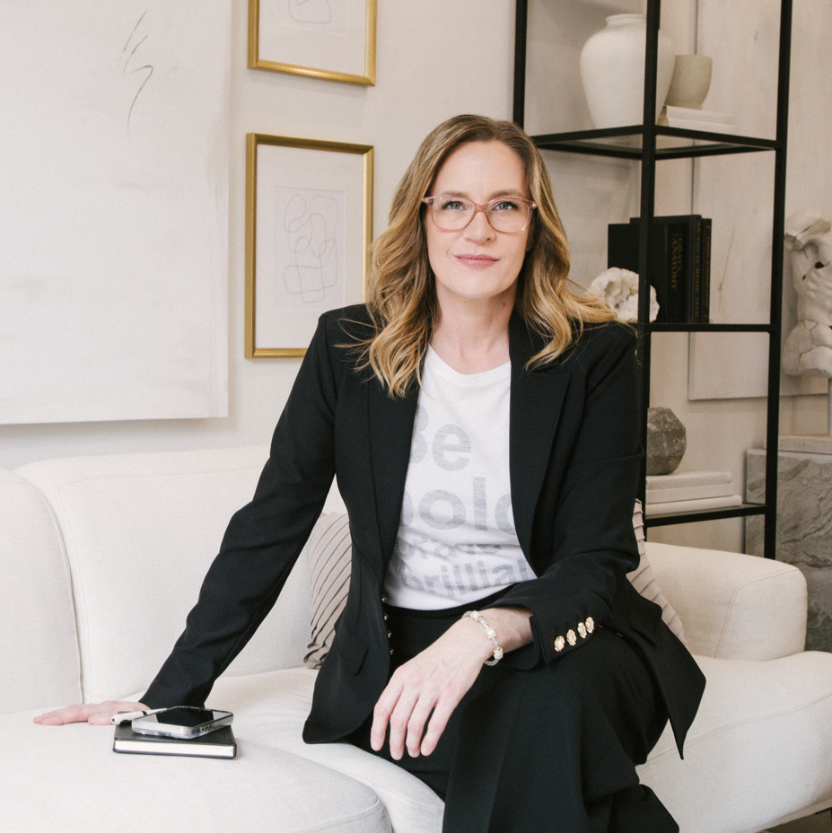 Allison Graham resilience speaker on a couch with a black blazer and a tshirt that says be bold be brave be brilliant