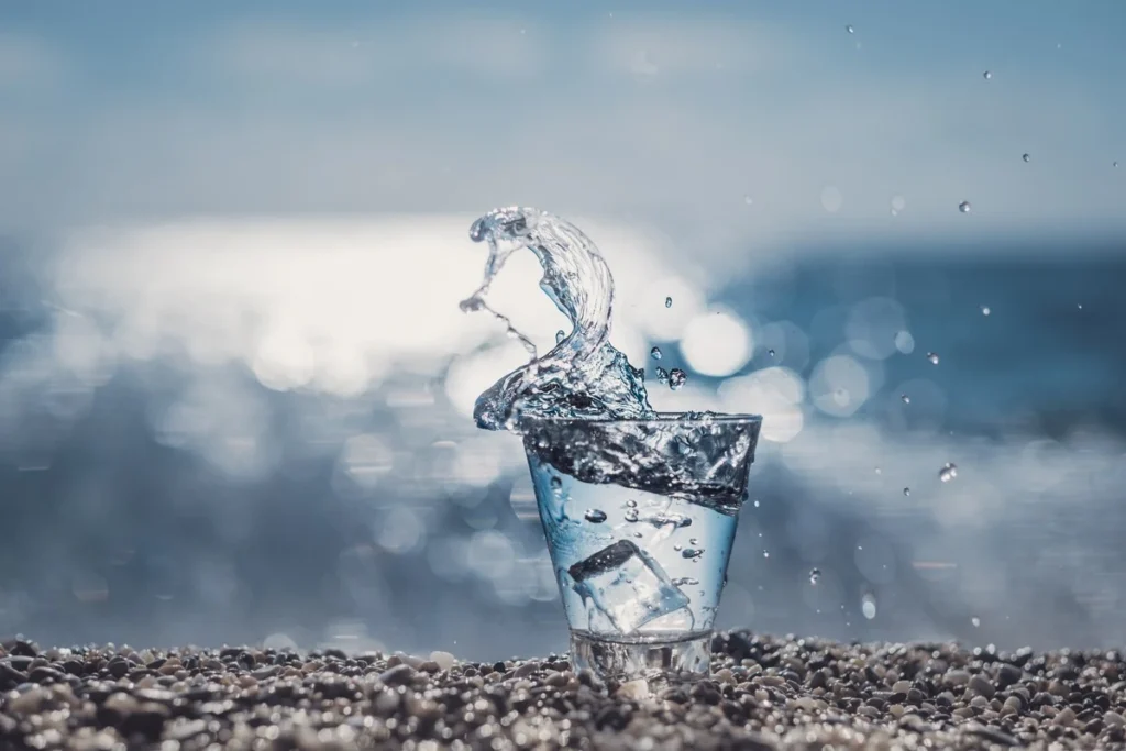 Glass of water overflowing with a splash on a pebbly beach representing capacity pushed beyond its limit