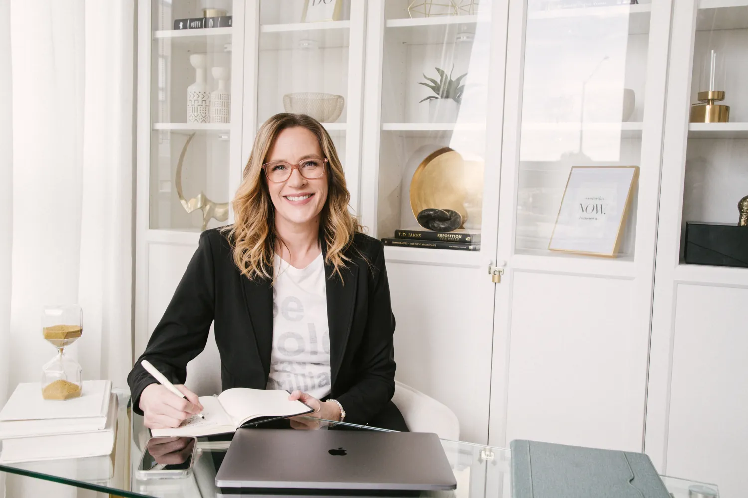 Allison Graham, capacity consultant, writing in a notebook at her desk with an hourglass beside her